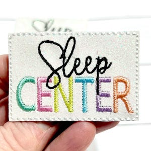 May include: A white iron-on patch with a rainbow embroidered design that says "Sleep Center".