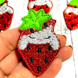 May include: Red glitter strawberry applique with green felt leaves and silver embroidered details. The strawberry has black seed details and a smiling face. Several strawberry appliques are visible.