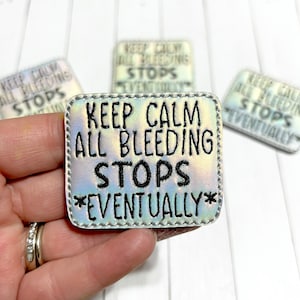 May include: A silver iridescent iron-on patch with black embroidery that reads "Keep Calm All Bleeding Stops *Eventually*"
