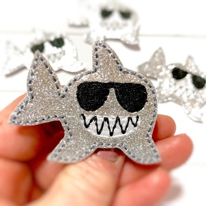 May include: Silver glitter shark applique with black embroidered sunglasses and teeth.