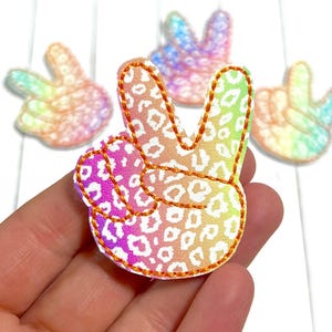 May include: Peace sign patches with a leopard print design in a rainbow gradient. The patches are outlined with orange stitching. Several patches are visible, with one in focus.
