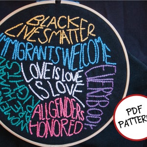 Peut inclure: Art de broderie sur un cercle avec le texte "Black Lives Matter", "Immigrants Welcome", "Love is Love", "All Genders Honored", et "Everybody", dans un arc-en-ciel de couleurs.