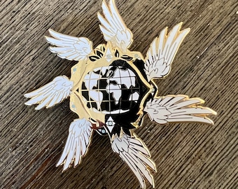 May include: A gold-toned enamel pin featuring a black and white globe surrounded by four white wings. The globe has a black and white design and a small eye on each side.