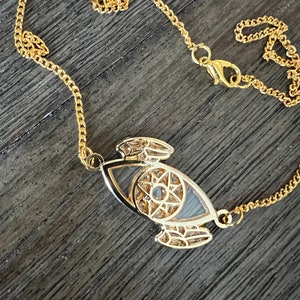 May include: A gold chain necklace with a detailed eye pendant. The eye is surrounded by a star and intricate designs.