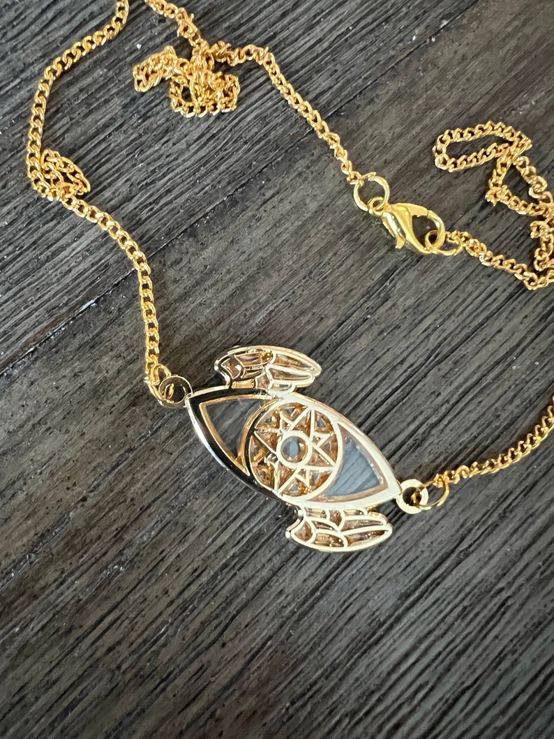 May include: A gold chain necklace with a detailed eye pendant. The eye is surrounded by a star and intricate designs.