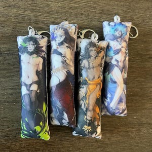 May include: Four rectangular plush keychains featuring anime-style character illustrations. Each soft fabric charm displays a unique figure with distinct color schemes including green, red, orange, and blue, all attached to silver metal key rings.