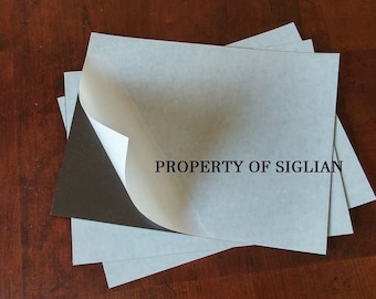 May include: A stack of four white adhesive-backed sheets with a black backing. The top sheet is partially peeled back to reveal the adhesive. The text "PROPERTY OF SIGLIAN" is printed on the white sheet.