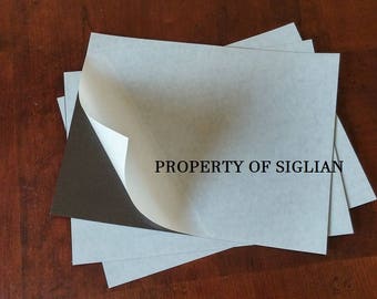 May include: A stack of white adhesive-backed paper sheets with a black backing. The top sheet is folded over to reveal the black backing. The text "PROPERTY OF SIGLIAN" is printed on the white sheet.