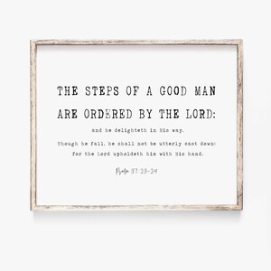 May include: A framed print with a white background and black text. The text reads "THE STEPS OF A GOOD MAN ARE ORDERED BY THE LORD: and he delighteth in His way. Though he fall, he shall not be utterly cast down: for the Lord upholdeth him with His hand. Psalm 37:23-24".