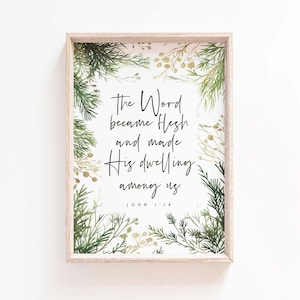 Op de afbeelding: Een ingelijste print met de tekst "The Word became Flesh and made His dwelling among us" uit Johannes 1:14. De tekst staat in zwart schrift op een witte achtergrond, omringd door groene en gouden botanische illustraties, en ingelijst in licht hout.