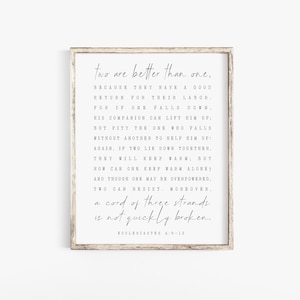 May include: A framed print with a white background and black text. The text is a quote from Ecclesiastes 4:9-12, which reads: "Two are better than one, because they have a good return for their labour. For if one falls down, his companion can lift him up: but pity the one who falls without another to help him up! Again, if two lie down together, they will keep warm; but how can one keep warm alone? And though one may be overpowered, two can resist. Moreover, a cord of three strands is not quickly broken."
