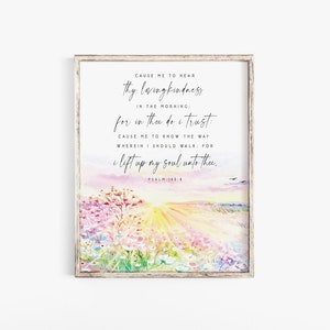 May include: A framed watercolour print with a quote from Psalm 143:8, depicting a pastel landscape. The artwork shows a sunrise over a field of flowers, with elegant script. The frame is made of light, natural wood.