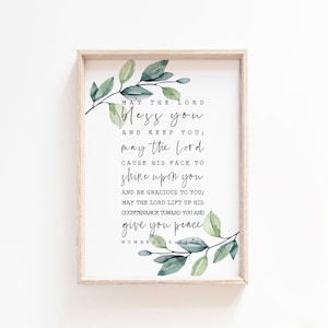 May include: A framed print with a white background and green watercolor leaves on the top and bottom. The print features a bible verse from Numbers 6:24-26, which reads: "May the Lord bless you and keep you; may the Lord cause his face to shine upon you and be gracious to you; may the Lord lift up his countenance toward you and give you peace."