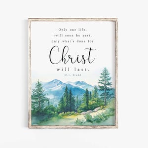 May include: A framed wall art print featuring a watercolour landscape of green pine trees and blue mountains. The text reads: Only one life, twill soon be past, only what's done for Christ will last. -C.T. Studd. The frame is a light brown wood.