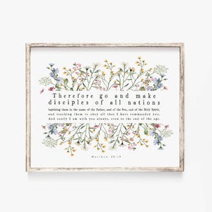 Könnte beinhalten: Ein gerahmter Druck mit einem hellen Holzrahmen. Der Druck zeigt den Text "Therefore go and make disciples of all nations" mit einem floralen Rand aus gelben, blauen und weißen Blumen. Der Text stammt aus Matthäus 28,19.