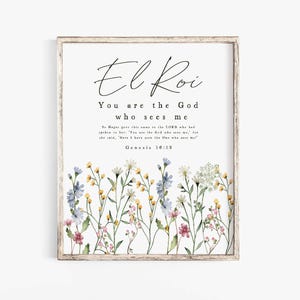 以下が含まれることがあります： 「El Roi」と「You are the God who sees me」という言葉がエレガントな筆記体で書かれた額入りのプリント。プリントの下部には、青、黄、ピンクの花を使った水彩画の花柄のデザインが施されています。フレームは明るい木の色です。
