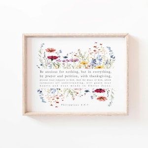 Può includere: Stampa incorniciata con un bordo floreale di fiori selvatici colorati in rosso, viola, giallo e blu. Il testo recita "Be anxious for nothing...Philippians 4:6-7". La cornice è in legno chiaro.