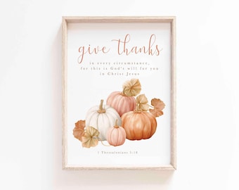 May include: A framed print with the words "give thanks" in a script font. Below the text are watercolor pumpkins in white, pink, and orange, with fall leaves. The text "1 Thessalonians 5:18" is at the bottom.
