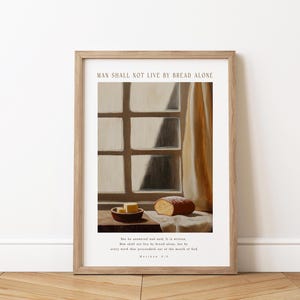 Puede incluir: Una impresión enmarcada con una pintura de una ventana con una cortina y una hogaza de pan y mantequilla sobre una mesa. El texto "El hombre no vivirá solo de pan" está en la parte superior de la impresión. El texto "Pero él respondió y dijo: Está escrito: El hombre no vivirá solo de pan, sino de toda palabra que sale de la boca de Dios." Mateo 4:4 está en la parte inferior de la impresión.