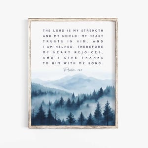 May include: A framed wall art print featuring a watercolor landscape of blue misty mountains and pine trees. The text reads: THE LORD IS MY STRENGTH AND MY SHIELD: MY HEART TRUSTS IN HIM, AND I AM HELPED. THEREFORE MY HEART REJOICES, AND I GIVE THANKS TO HIM WITH MY SONG. Psalm 28:7.