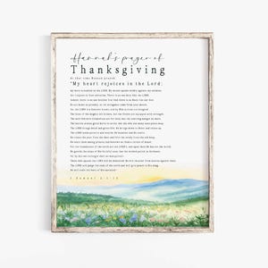 Può includere: Stampa incorniciata con il testo "Hannah's prayer of Thanksgiving" e un paesaggio ad acquerello. Il testo è in stile manoscritto e il paesaggio presenta un campo di fiori e una catena montuosa.