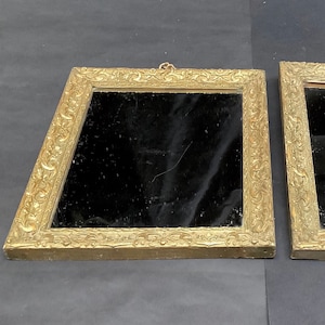 May include: Two ornate gold-coloured picture frames with black velvet backing. The frames have a decorative, intricate design.