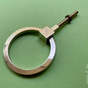 May include: A silver ring pull handle with a square base and a screw. The handle is on a green background.