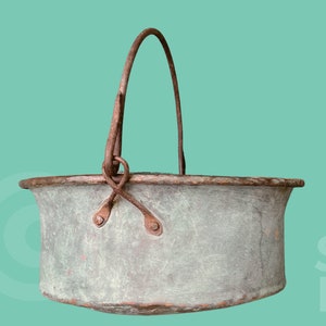 May include: A vintage copper bucket with a rusty metal handle. The bucket is oval shaped and has a worn, green patina.