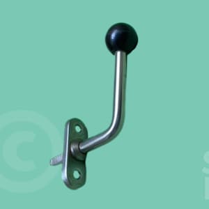 May include: A metal wall hook with a curved arm and a black ball at the end. The hook is mounted on a rectangular plate with two holes for screws. The background is a solid teal color.