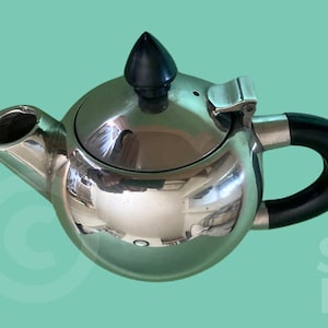 May include: A shiny, silver-colored teapot with a black handle and lid finial. The teapot has a rounded body and a spout on the left side. The background is a light teal color with the text "BRIQUE STUDIO" in white.