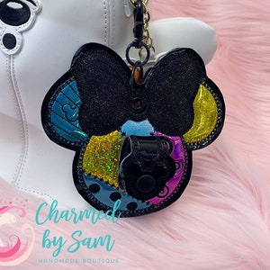 May include: A colorful patchwork-style Minnie Mouse head keychain with a black bow and a black charm. The keychain is attached to a silver chain.