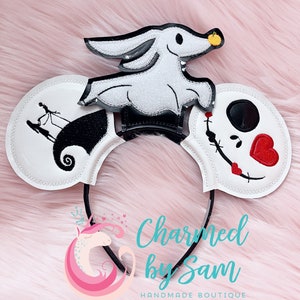 May include: White mouse ears with black embroidery of Jack Skellington and Sally from The Nightmare Before Christmas. The right ear features a red heart and a black stitched smile. The left ear features a black silhouette of Jack and Sally on a hill. A white ghost dog with black eyes and a black stitched mouth is attached to the headband. The headband is black. The text "Charmed by Sam" is visible below the headband.