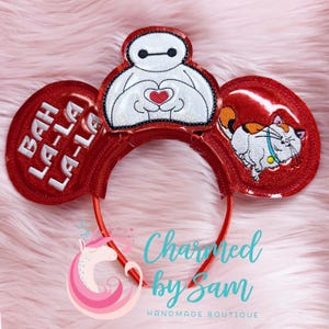 May include: Red Minnie Mouse ears with a white Baymax character holding a red heart, a white cat with orange and black markings, and the text "Bah La-La La-La" on the left ear.