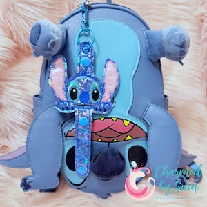 May include: Blue Stitch backpack with a blue and pink Stitch character keychain. The keychain has a sparkly iridescent strap.