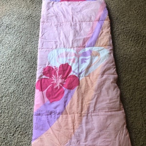 May include: A pink and purple sleeping bag with a floral design. The sleeping bag has a zipper and a hood.