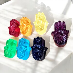 May include: Seven colourful hamsa hand charms in red, orange, yellow, green, blue, purple and dark blue. The hamsa hands are a popular symbol of protection and good luck.