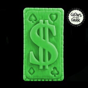 May include: A green glow-in-the-dark playing card with a dollar sign on it. The card has a textured surface and a border with four leaf clover symbols.