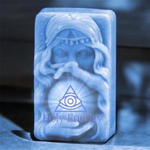 May include: A blue soap bar with a raised image of a woman's face and a triangle with an eye inside. The text "Holy Energy" is printed below the image.