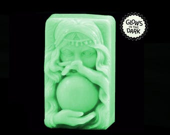 May include: A green soap bar with a woman's face and a glowing orb in her hands. The soap glows in the dark. "Glows in the Dark" is written on a starburst sticker.