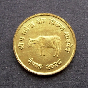 May include: A gold-coloured coin with the text "Nepal 2026" and an image of a cow. The text around the cow reads "Sarva Dharma Sambhava"