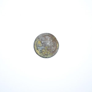 May include: A tarnished, antique coin with the word "SLUBER" arched across the top. The coin has a worn appearance, with visible text and design elements. The coin's edges show signs of wear and age.