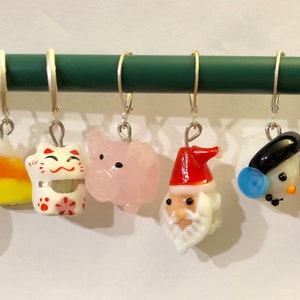 Puede incluir: Ocho adornos de vidrio coloridos colgando de una varilla plateada. Los adornos incluyen una piña, un maíz dulce, un gato de la suerte, un cerdo, Santa Claus, un muñeco de nieve y un bastón de caramelo.