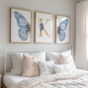 Set of 3 blue and gold butterfly prints, personalized with a letter of your choice, unframed, the picture shows how the triptych looks once framed in a girl bedroom over the bed, displayed size A3 and displayed initial K