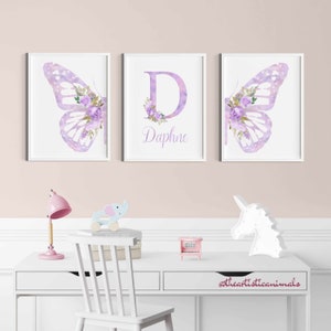 Op de afbeelding: Drie ingelijste prints met een aquarel vlinderontwerp. De middelste print heeft de letter "D" met de naam "Daphne" eronder. De prints zijn in een witte lijst met een witte achtergrond.