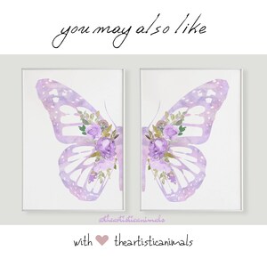 Op de afbeelding: Twee aquarel-vlinderprints met paarse bloemen en een lichtpaarse achtergrond. De prints zijn ingelijst in witte lijsten en worden getoond op een witte muur. De tekst "theartisticanimals" staat onderaan de afbeelding.