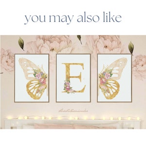 May include: Three framed art prints with gold butterfly wing and letter "E" designs. The butterfly wings and letter are adorned with floral arrangements in pink, purple, and white. The background features a floral pattern and the text "you may also like".