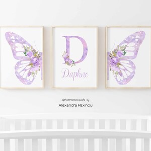 Op de afbeelding: Drie aquarelprints met een paarse vlinder met bloemmotieven, de letter D met bloemmotieven en de naam Daphne. De prints zijn ingelijst in een licht houten lijst.