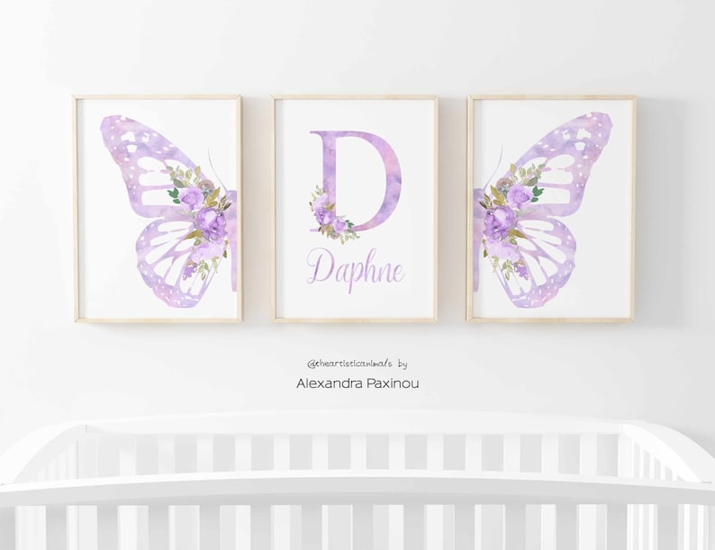 Op de afbeelding: Drie aquarelprints met een paarse vlinder met bloemmotieven, de letter D met bloemmotieven en de naam Daphne. De prints zijn ingelijst in een licht houten lijst.