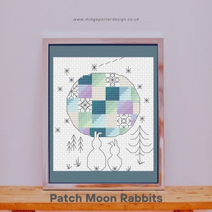 May include: A cross-stitch pattern featuring two rabbits holding a patchwork moon with a blue, green, and purple color scheme. The moon is surrounded by stars and small trees. The text "Patch Moon Rabbits" is below the image.