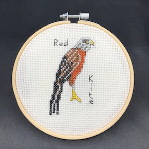 May include: A cross-stitch embroidery of a red kite, with the words "Red Kite" stitched below the bird.